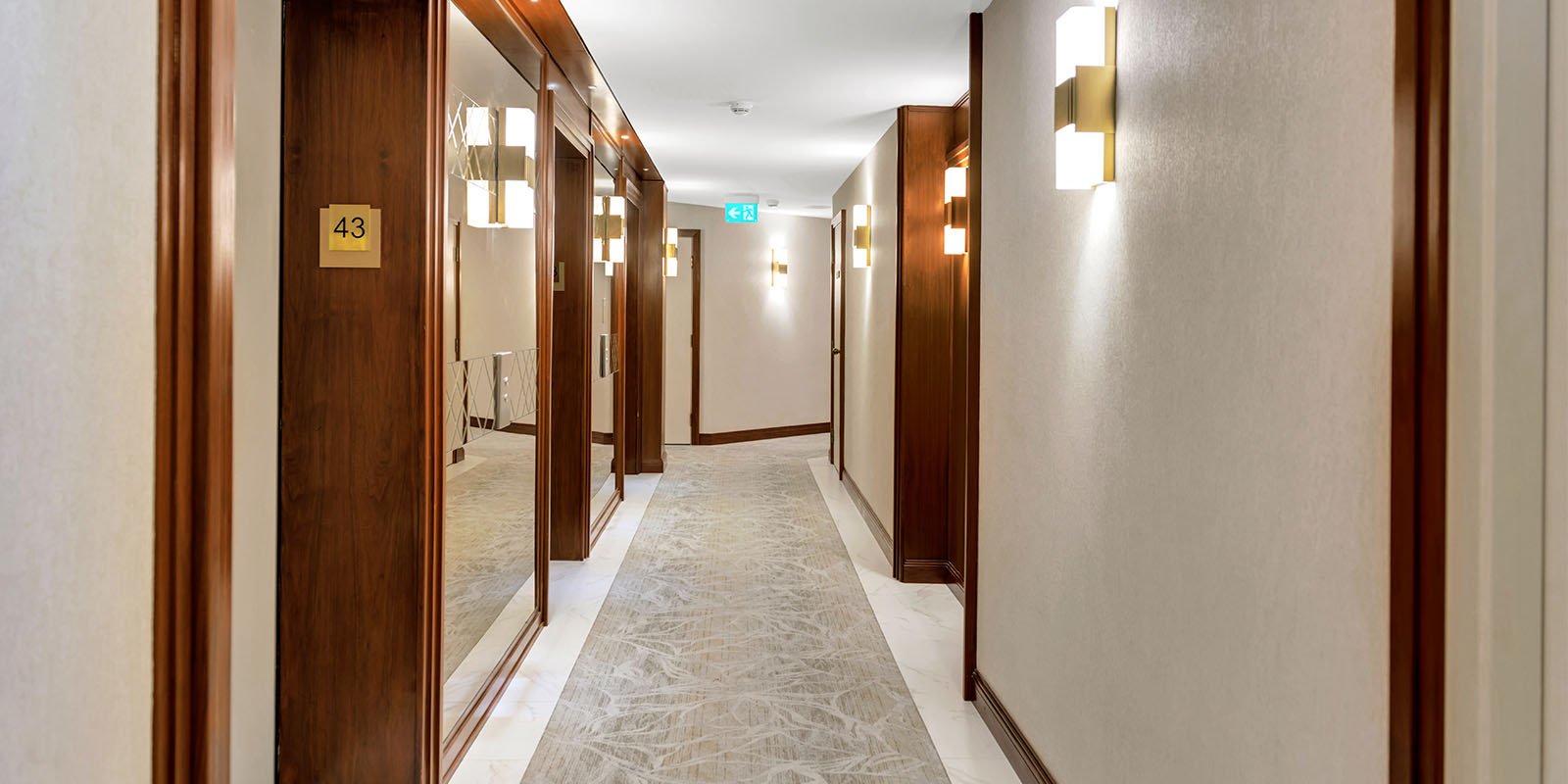 Refurbished condo corridor in Toronto with new wall panelling, patterned broadloom, wall base and recessed lighting