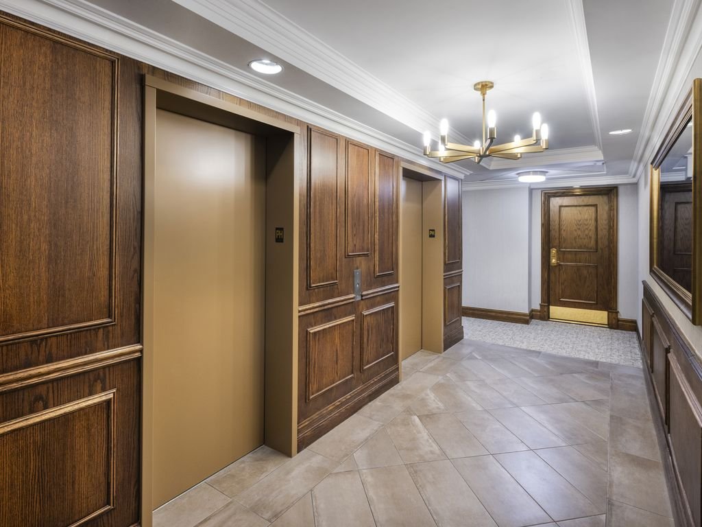 Refreshed Kensington at Old Mill II elevator lobby with a brass chandelier, wood panelling and wood doors