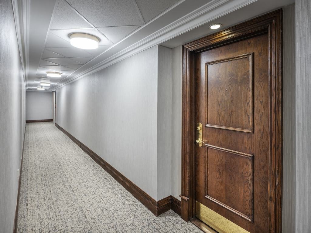 Long Kensington at Old Mill II corridor with patterned carpet, light wallpaper and a wood door with brass kickplate