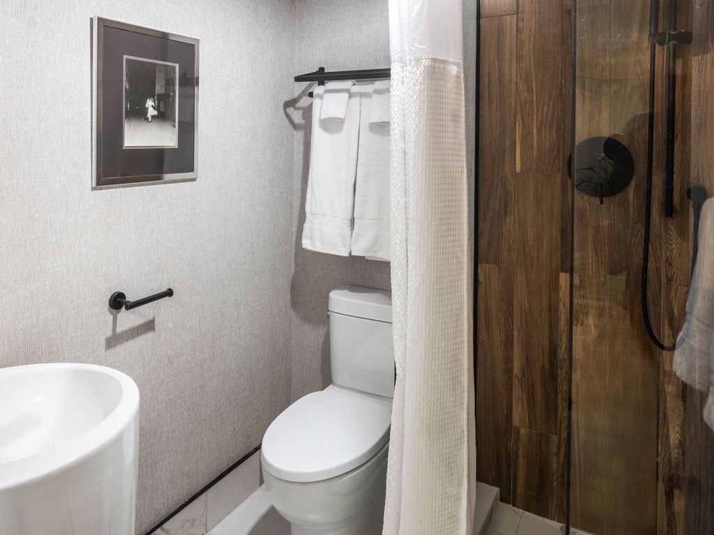 New bathroom at 250 Queens Quay with white fixtures, towels and a dark wood-look shower wall