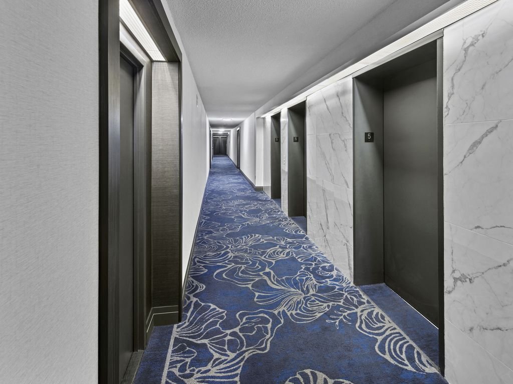 Renovated Platinum on The Humber II corridor with marble-look tile, dark door frames and blue patterned carpet