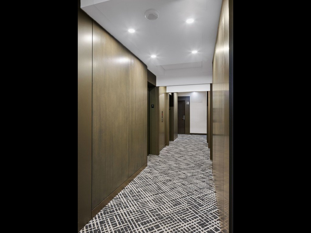 Refurbished X2 Condos corridor with a two-tone geometric carpet, bronze-toned wall panels and elevator doors