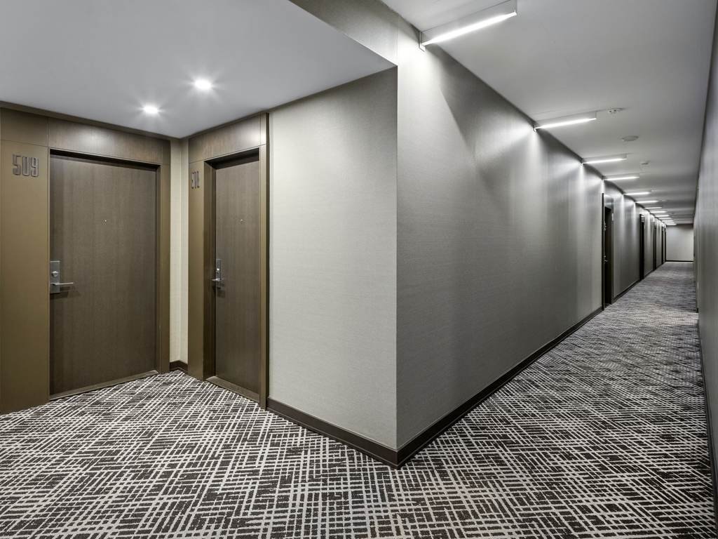 Long X2 Condos corridor with grey wall covering, dark door frames and continuous two-tone carpet