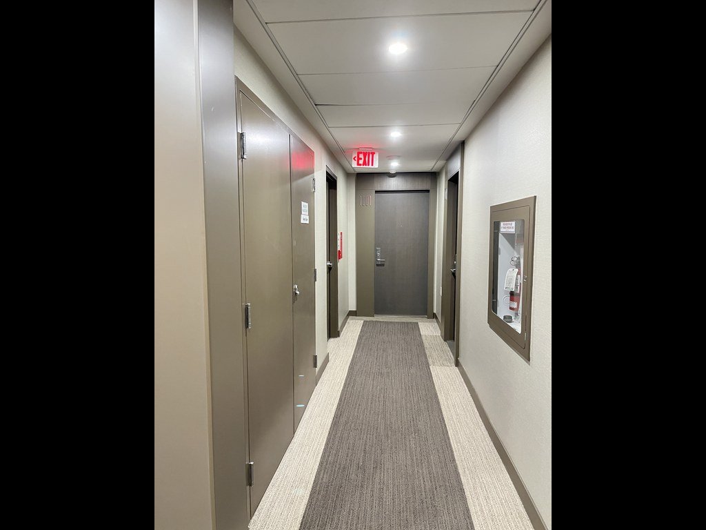 X2 Condos corridor before refurbishment with an exit sign, fire cabinet and bordered runner carpet