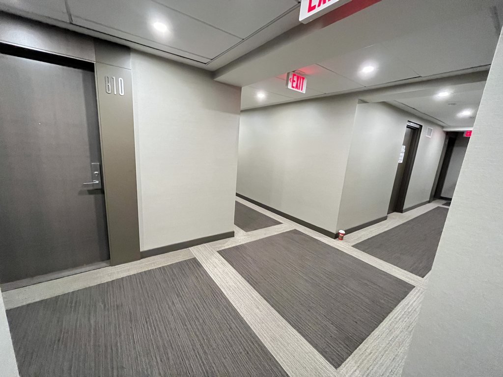 X2 Condos corridor corner before refurbishment with a bordered grey carpet and exit sign