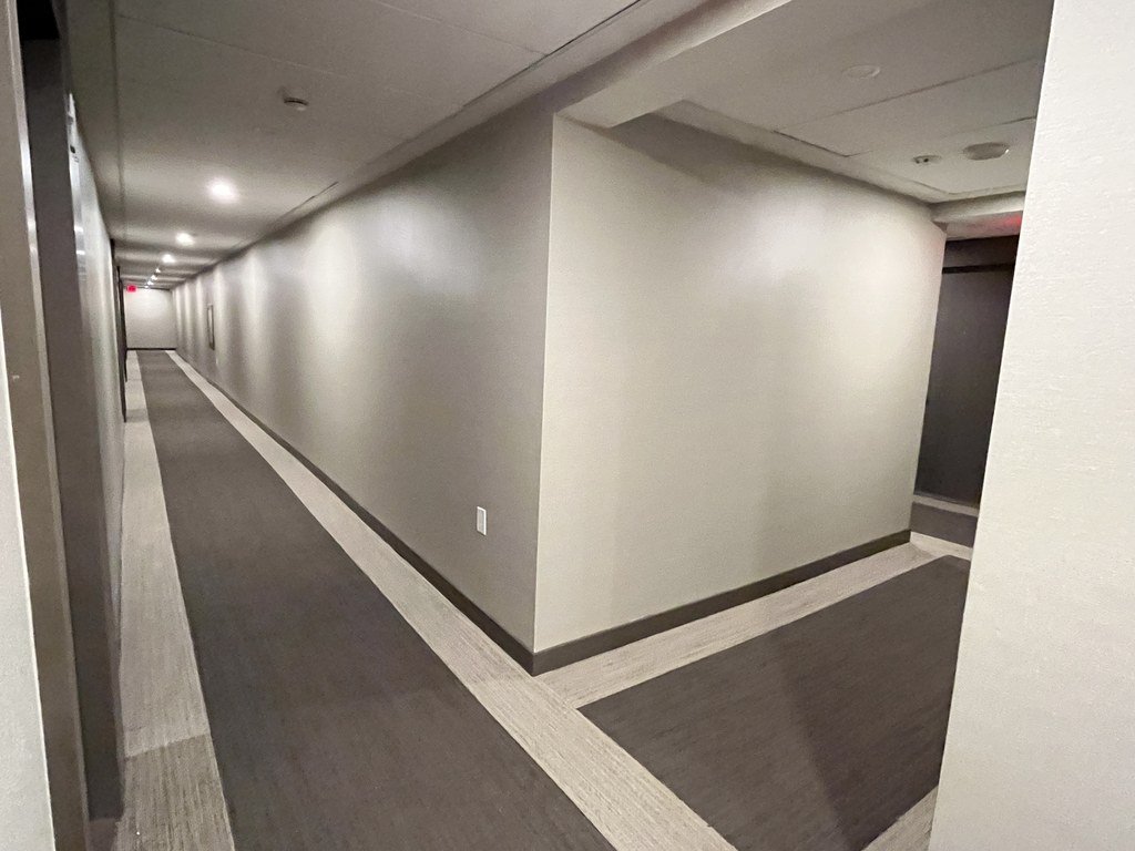 Long X2 Condos hallway before refurbishment with a grey runner carpet and pale borders