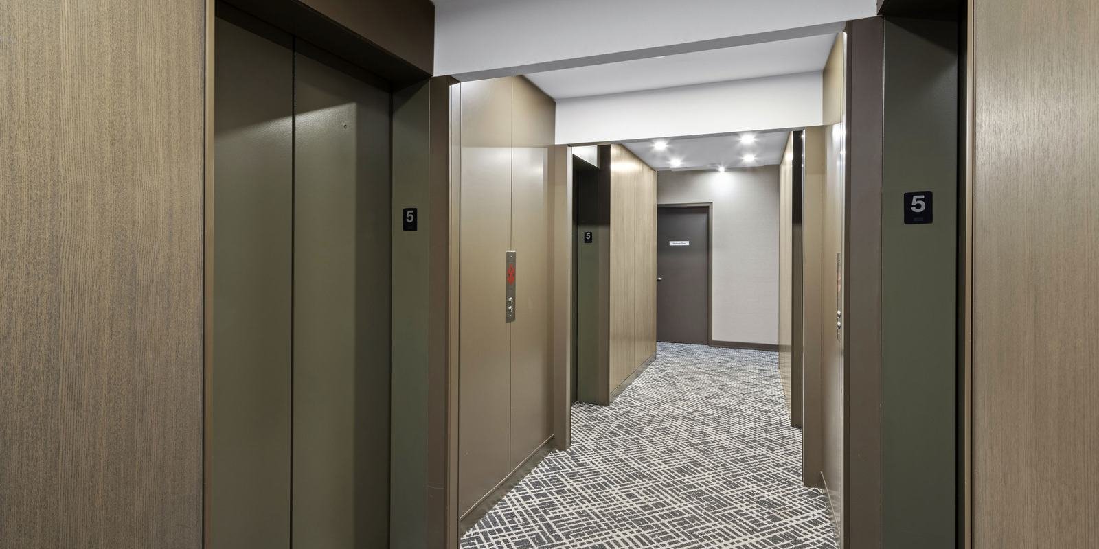 X2 Condos hallway after refurbishment with new patterned carpet, warm bronze panelling and elevator doors