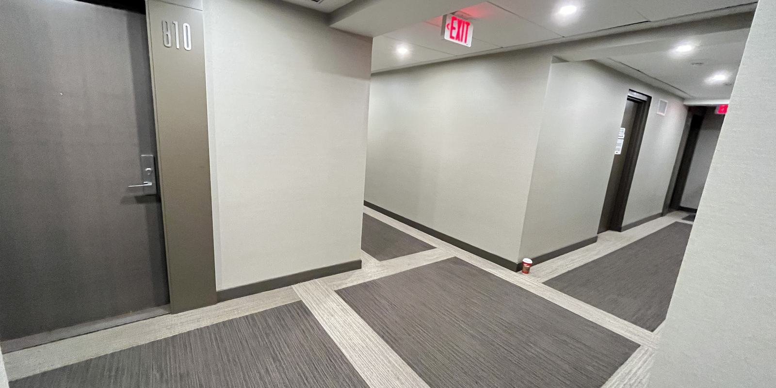 X2 Condos corridor corner before refurbishment with a bordered grey carpet and exit sign