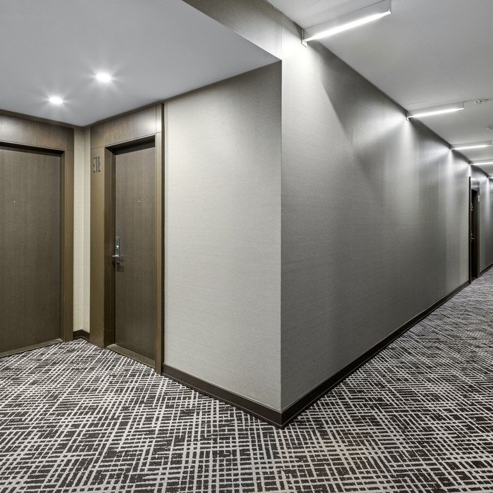 Long X2 Condos corridor with grey wall covering, dark door frames and continuous two-tone carpet